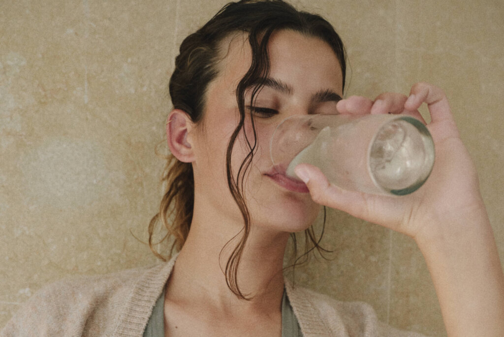 Woman drinking from a glass in warm natural light, representing a daily wellness ritual