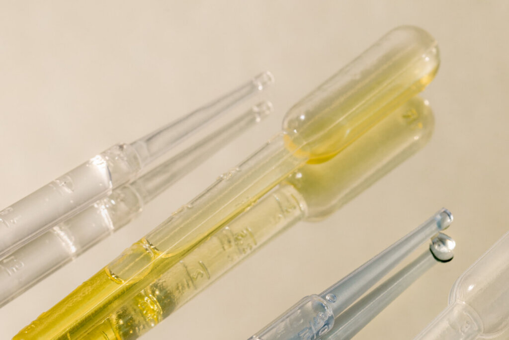 Glass pipettes with amber liquid on a warm neutral background, representing precision science and biotech firsts