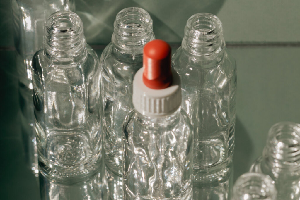 Cluster of clear glass bottles with a dropper cap, on a sage green background, representing the many related families within collagen